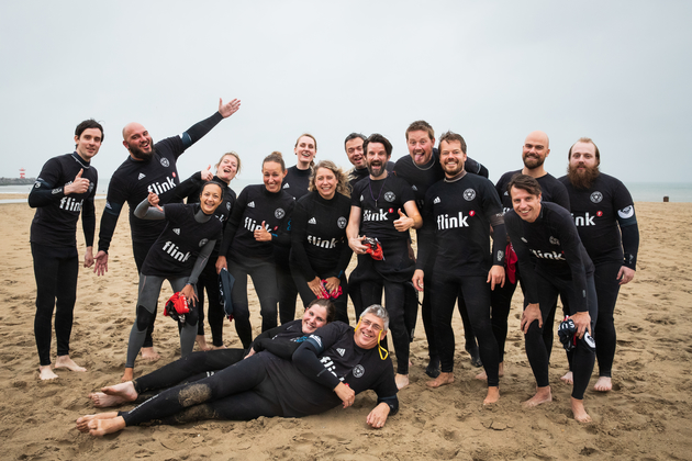 Teamuitje groepsfoto van alle Flinkerts in wetsuits op het strand