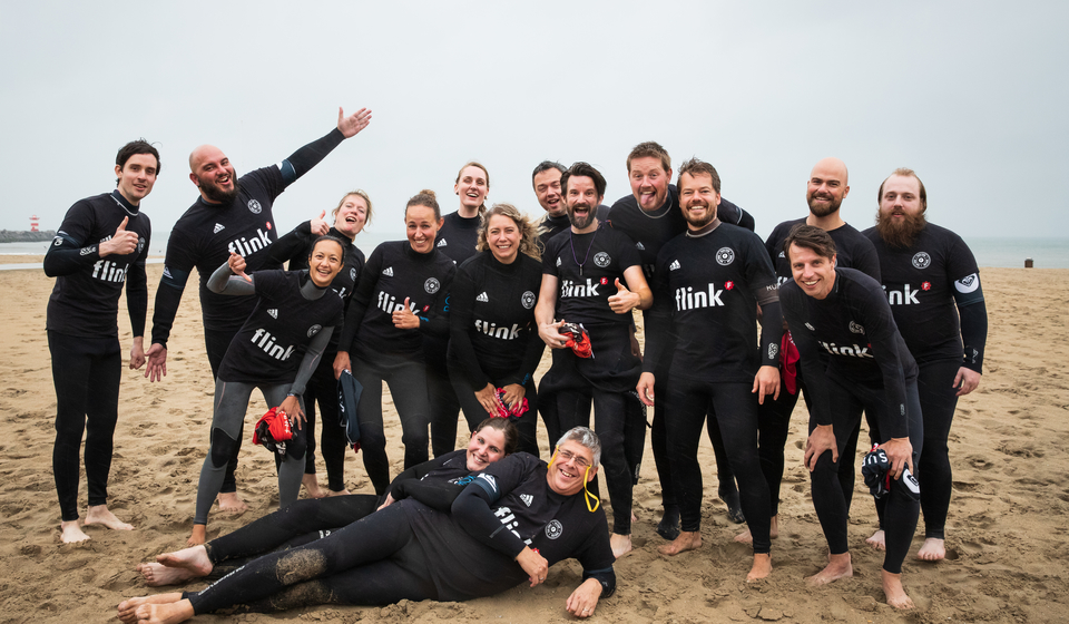 Teamuitje groepsfoto van alle Flinkerts in wetsuits op het strand